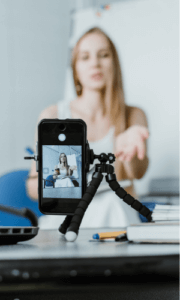 woman in the background speaking to the camera, with a smartphone on a tripod recording the woman